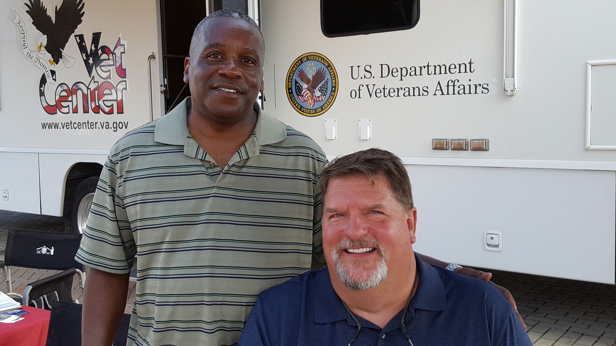 VA health expert poses with Veteran in front of a Mobile Vet Center