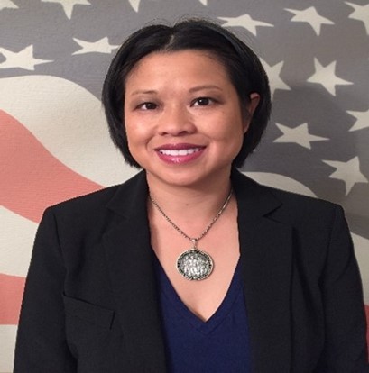 srey austin with short dark hair with black jacket and black blouse posing in front for american flag backdrop