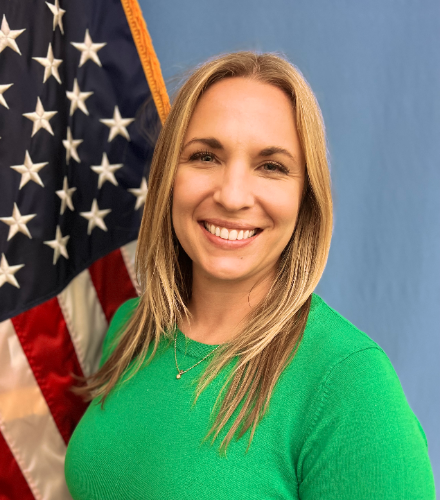 kate schoenlein with long straight blond hair  and green blouse posing in front of american flag with blue background