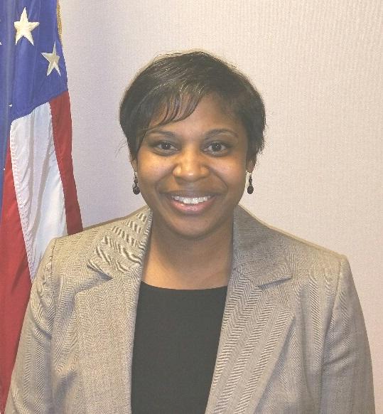 Carolyn poses in front of United States flag wearing a light gray jacket and black blouse